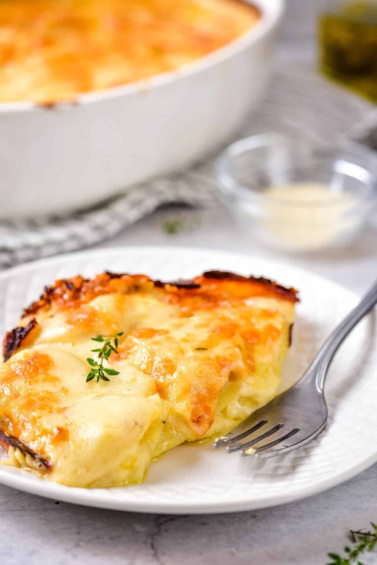 A melty piece of potatoes au gratin on a white plate with a fork.