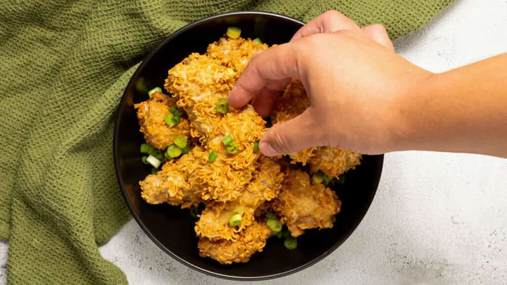 ramen fried chicken in a black bowl with a hand picking up a piece.