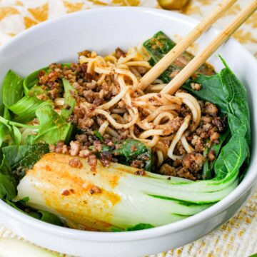 dan dan noodles in a white bowl with chopsticks.