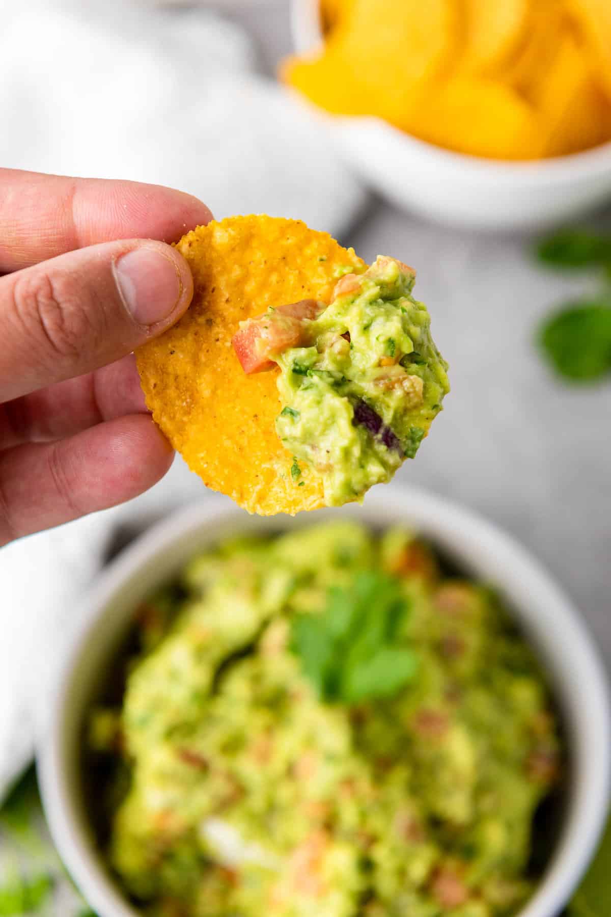 Hand holding a chip with guacamole on it.