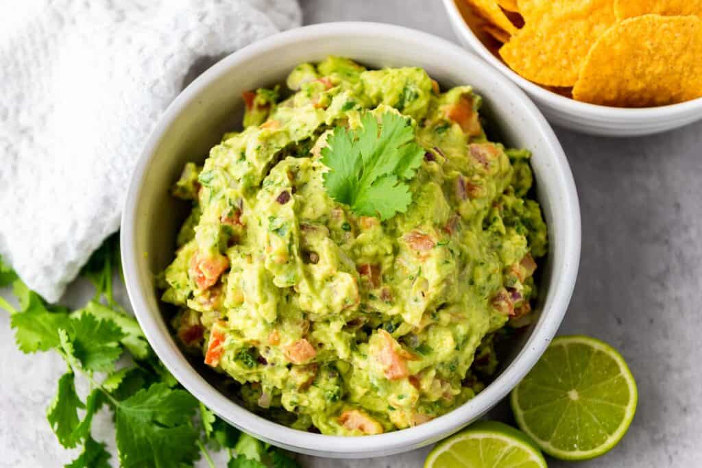 Guacamole in a white bowl with chips on the side.