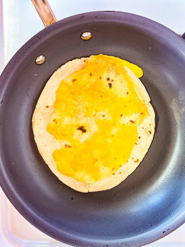 roti in a skillet with egg spooned over the top.
