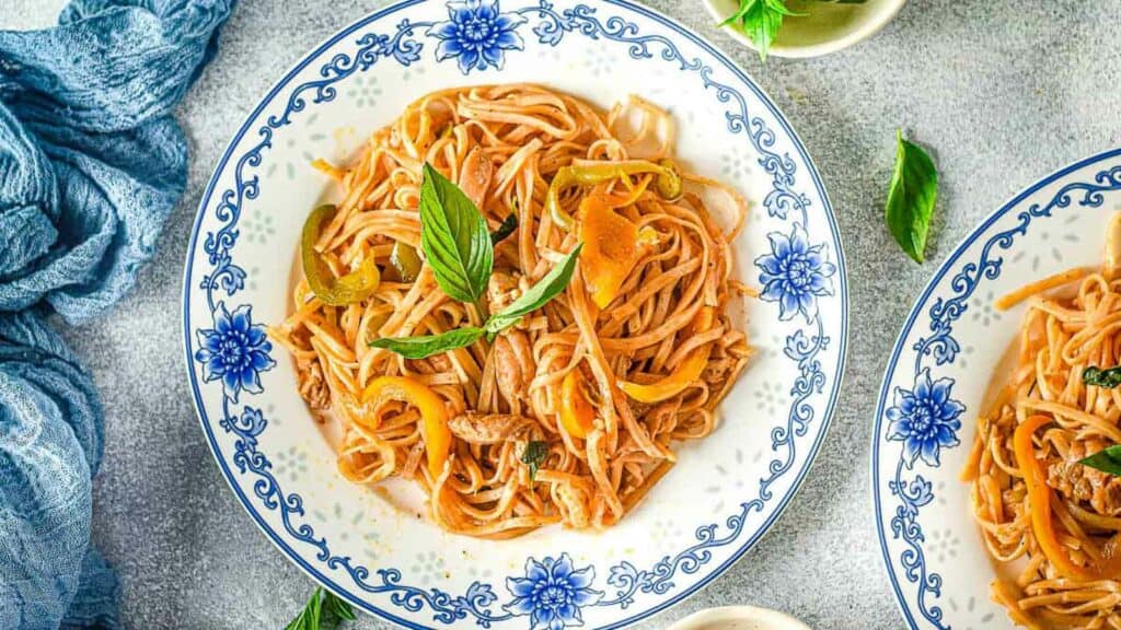 Two plates of noodles with peppers and basil on a gray background.