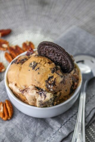 Mississippi mud ice cream in a white bowl with an oreo stuck in the ice cream and a spoon and pecans on the side.