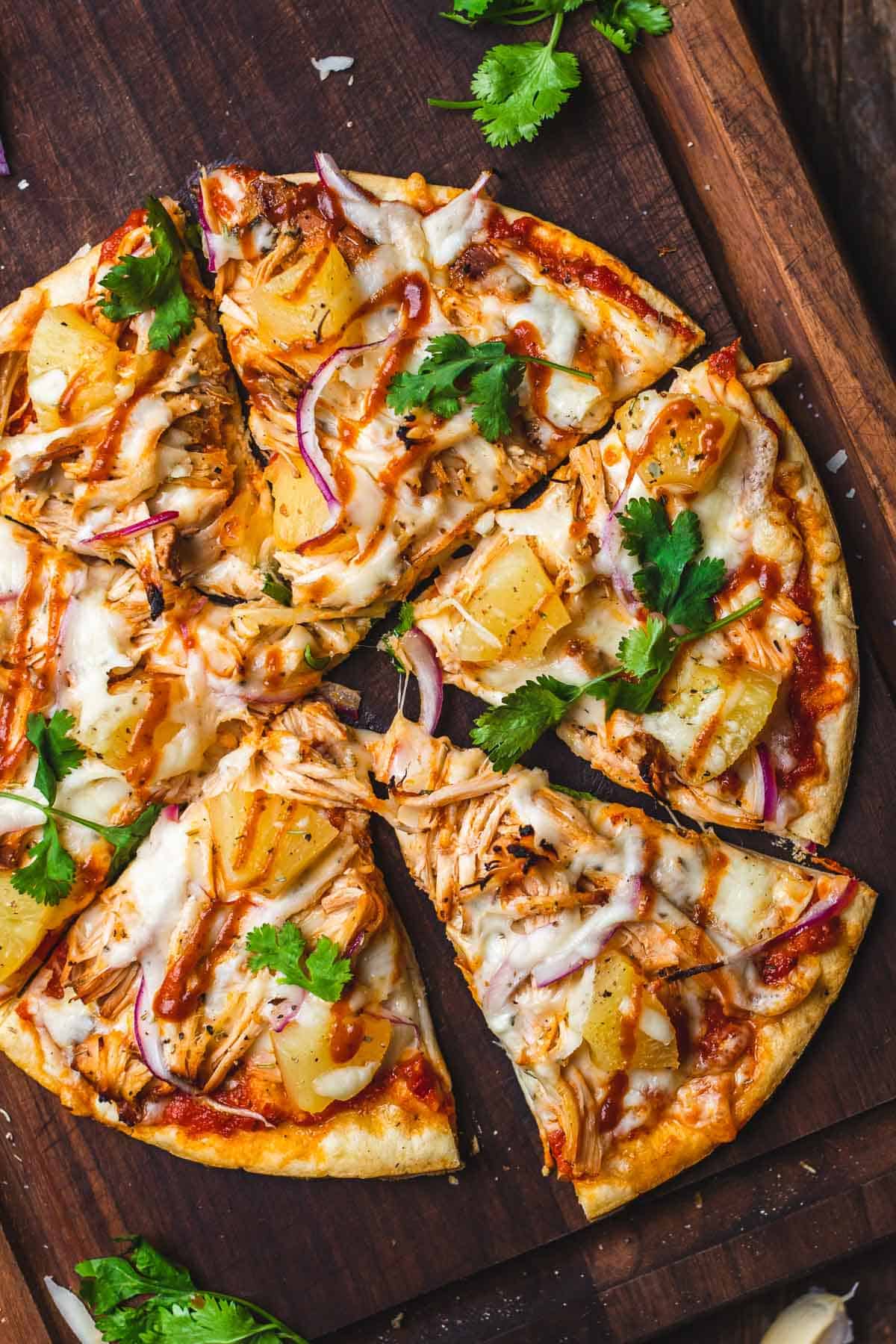 overhead shot of a pizza ith pineapple, chicken, barbecue sauce, red onions, and cilantro.