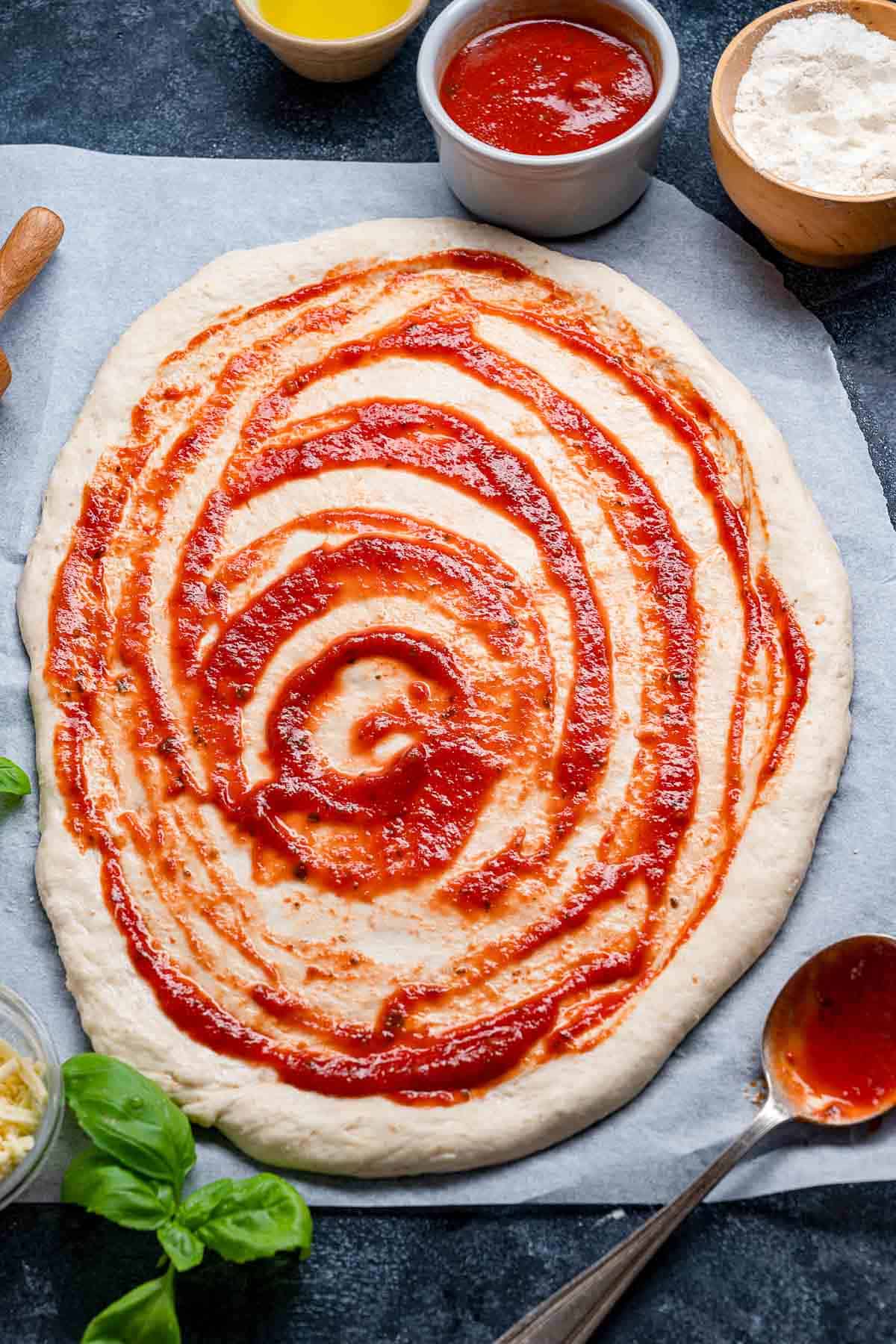 overhead shot of a round of pizza dough topped with tomato sauce.