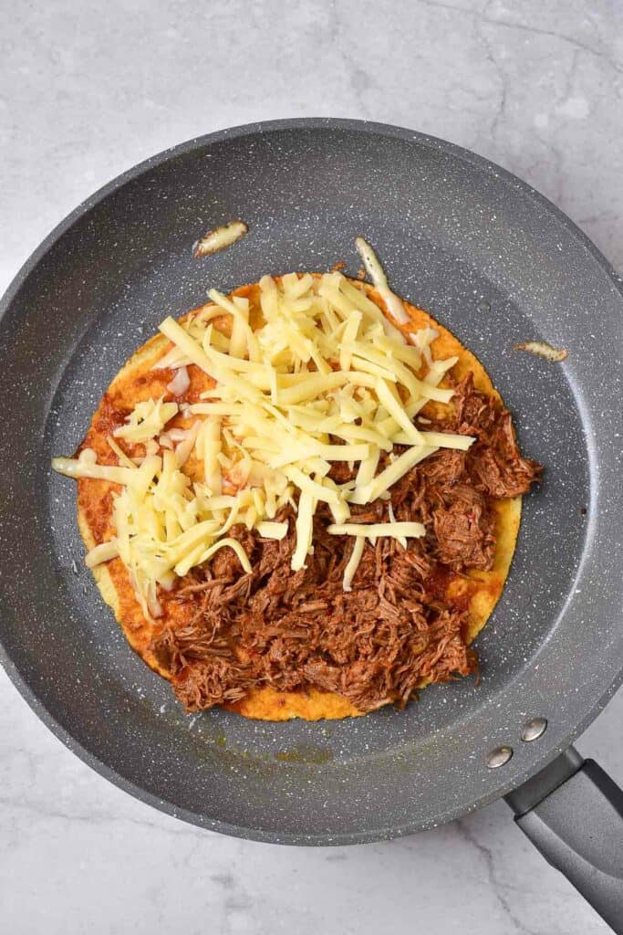 tortilla with birria and cheese in a skillet.