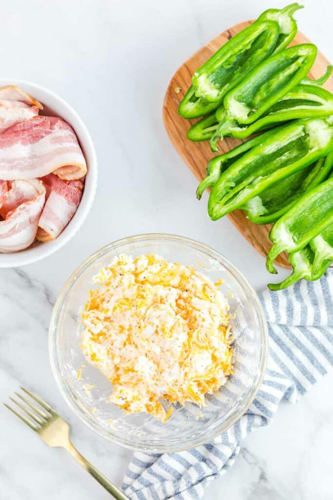 A bowl of cheese, bacon and green peppers next to a fork.