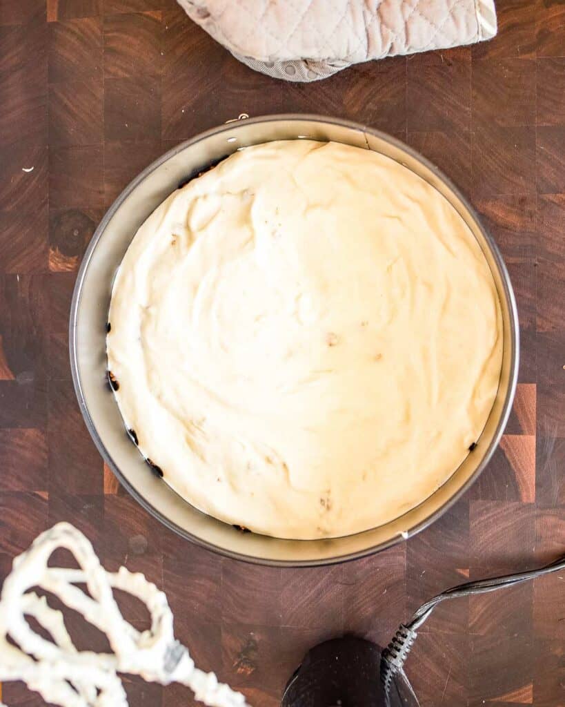 A white cake in a pan next to a whisk.