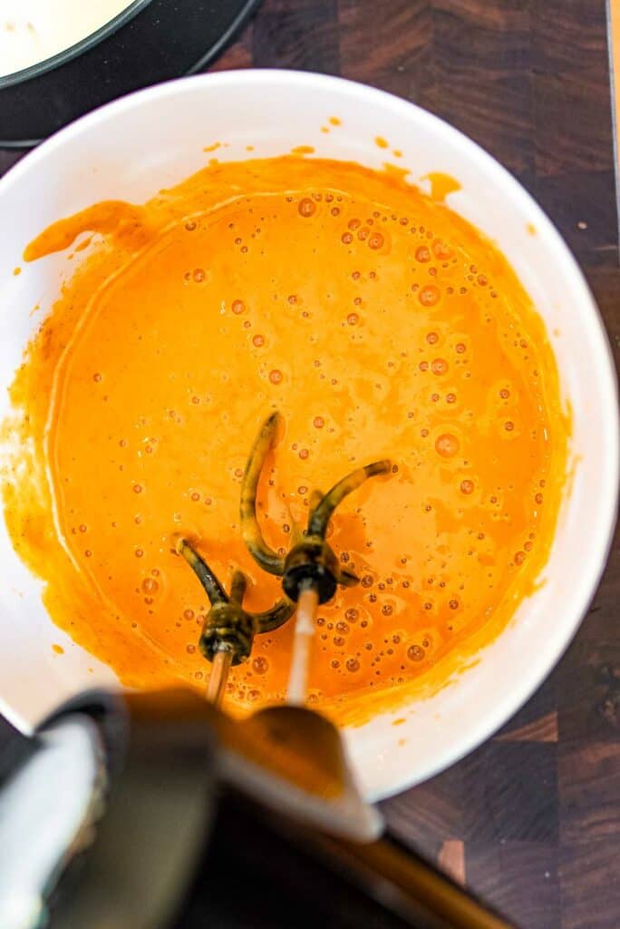 A bowl of orange sauce with a blender in it.