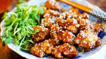 Low angle shot of a plate of fried chicken with sesame sauce and sesame seeds.