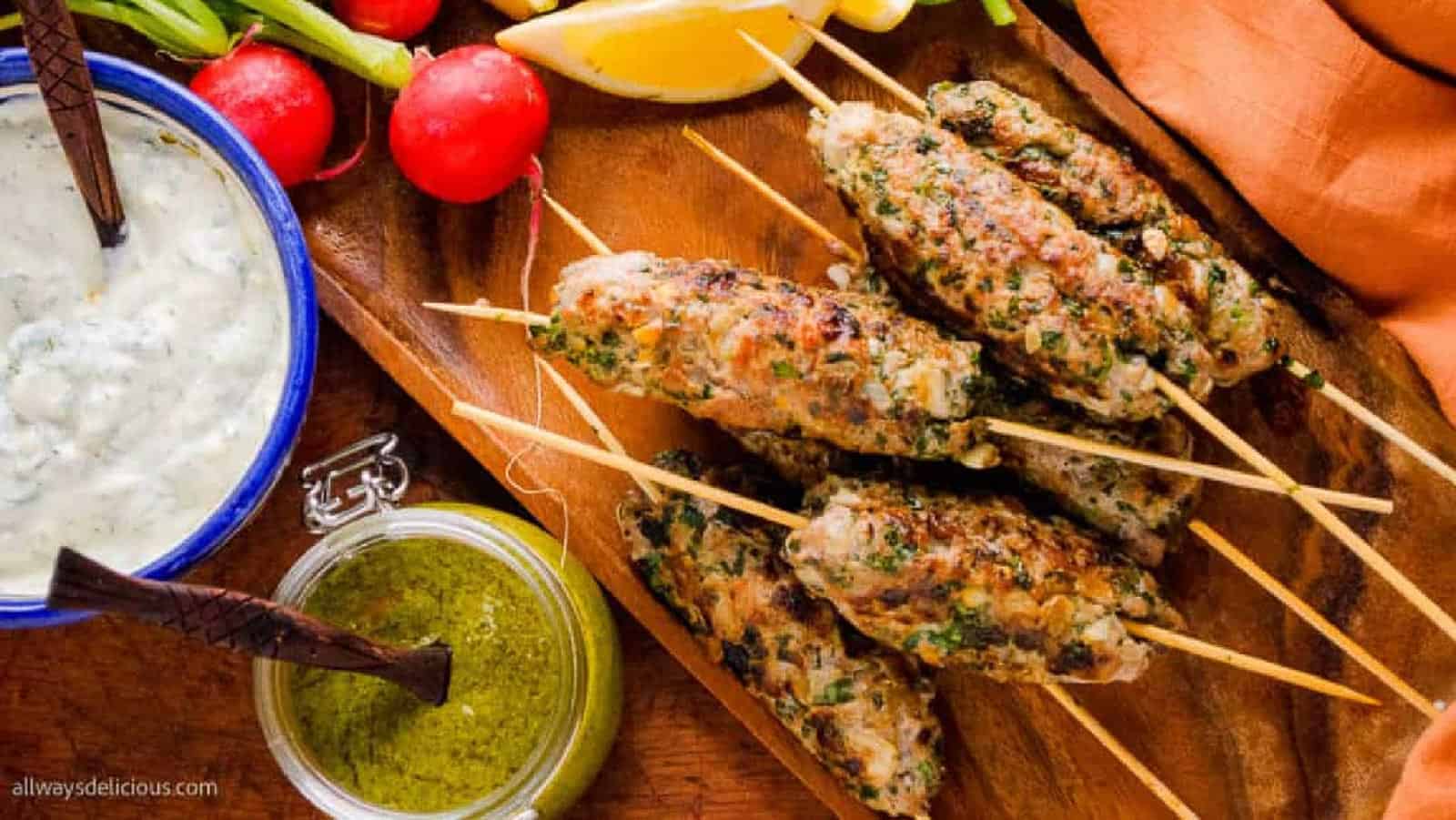 Lamb kofta kebabs on a wooden board with  fresh herbs and vegetables.