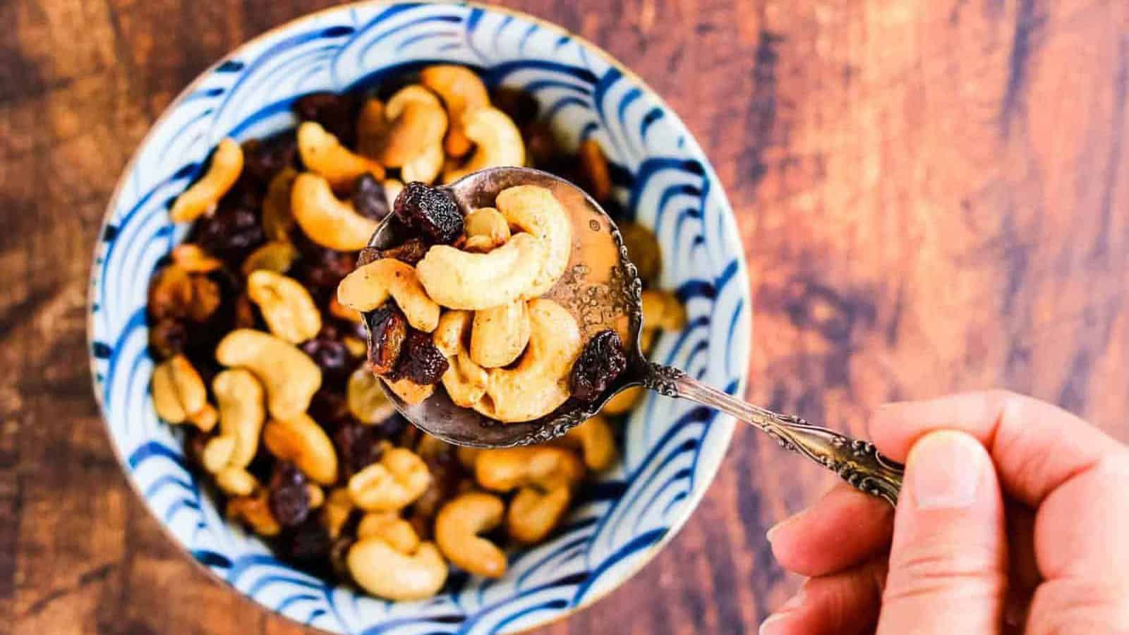 Caramelized cashews and raisins in a bowl with a silver spoon being lifted.