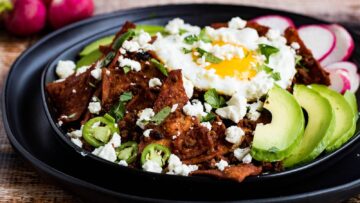 Overhead shot of chilaquiles on a black plate with a fork and knife on the side.