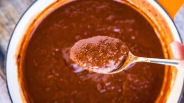 Overhead shot of a pot of enchilada sauce witih a spoonful of enchilada sauce above it.