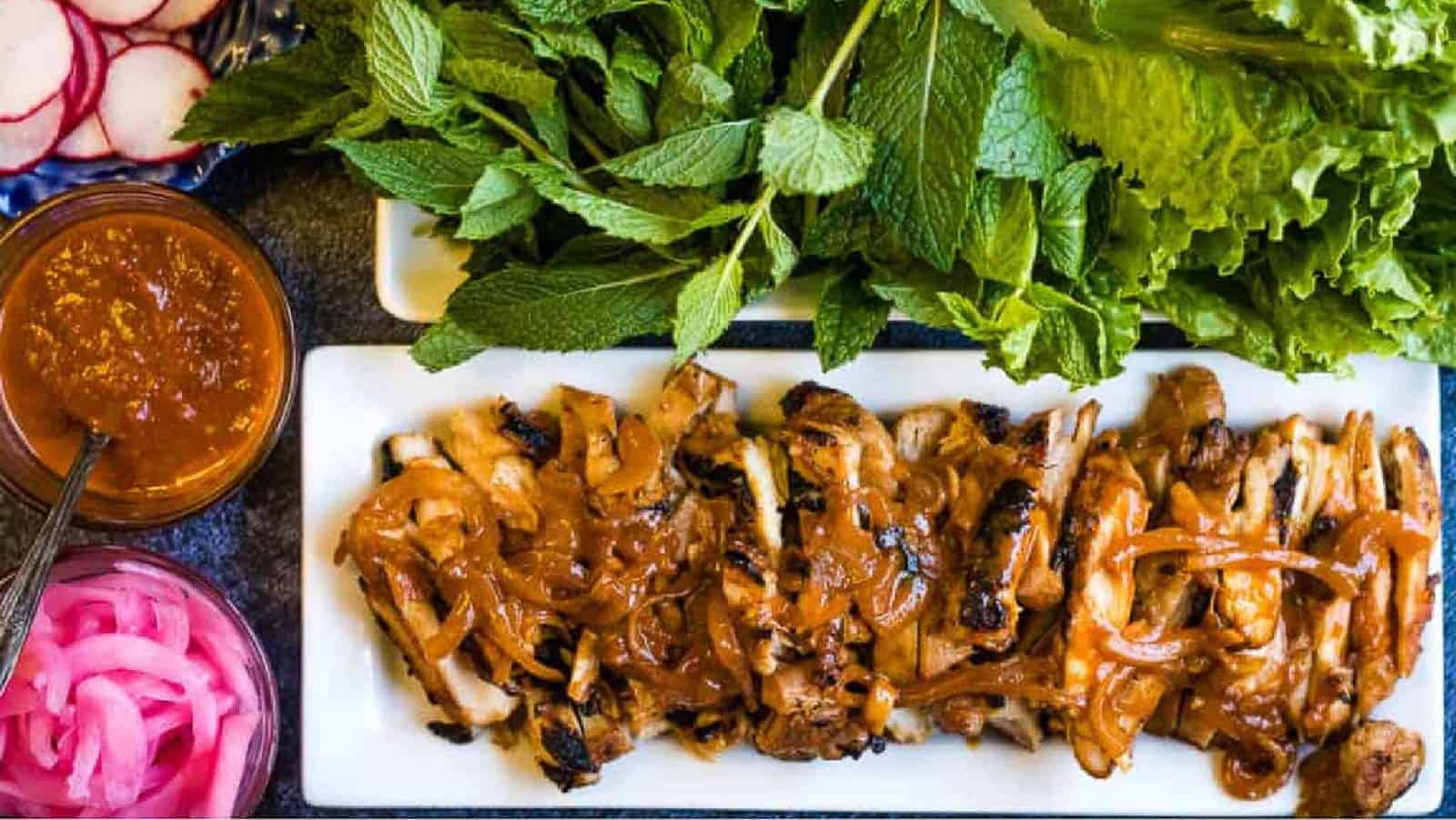 Gochujang chicken on a platter with fresh herbs.
