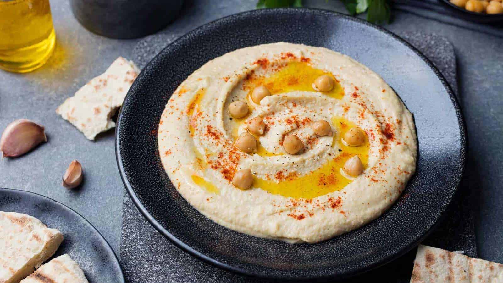 Hummus in a black bowl garnished with whole chickpeas, olive oil, and paprika.