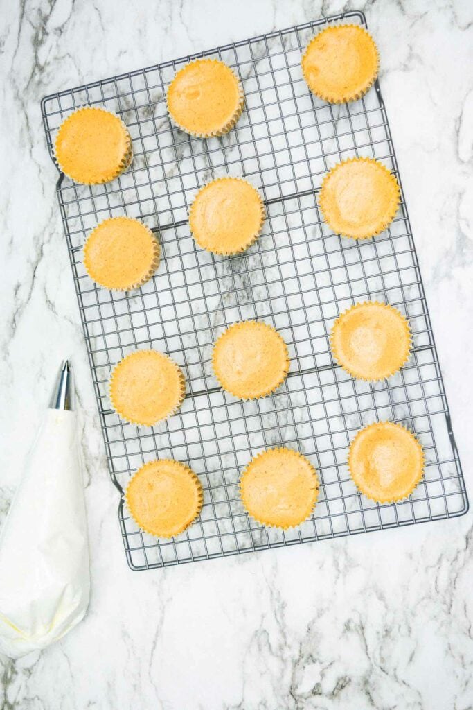 A cooling rack full of mini pumpkin cheesecakes on a marble countertop.