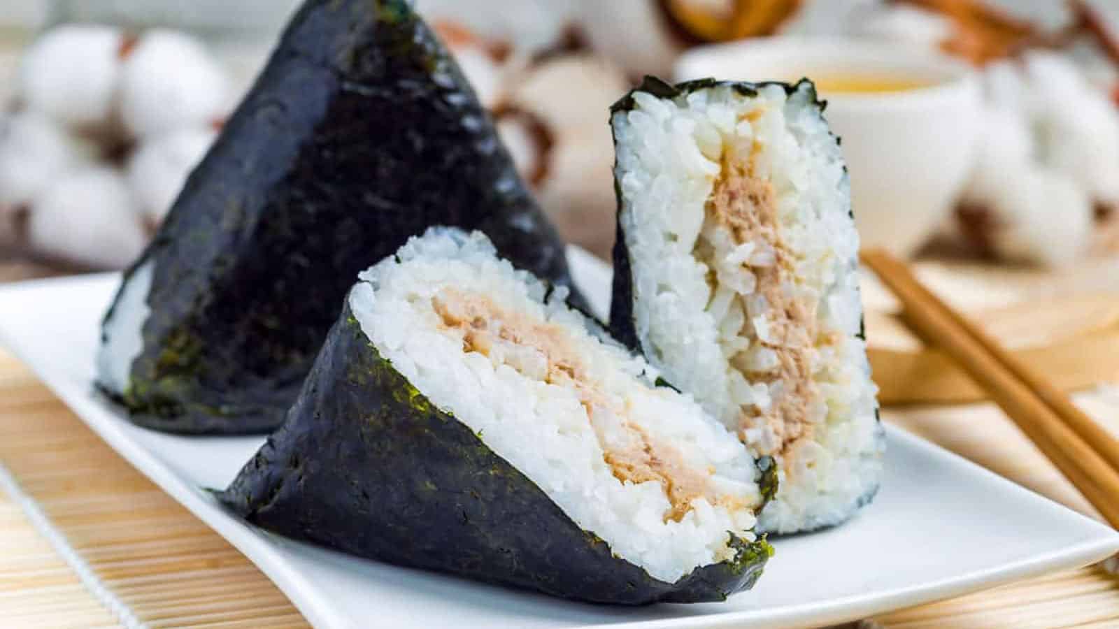 Two pieces of onigiri on a plate with chopsticks.