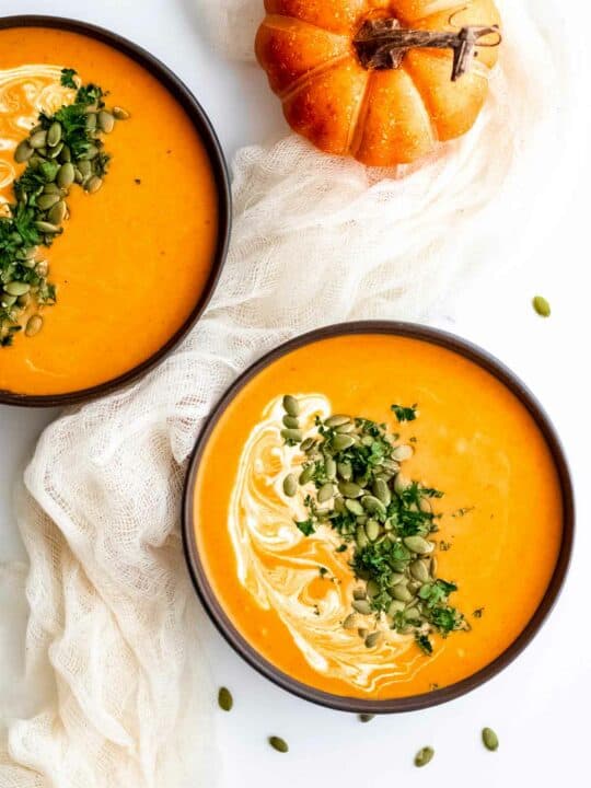 Two bowls of pumpkin soup on a white cloth.