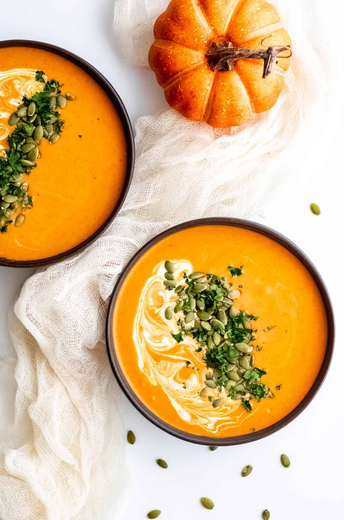 Two bowls of pumpkin soup on a white cloth.