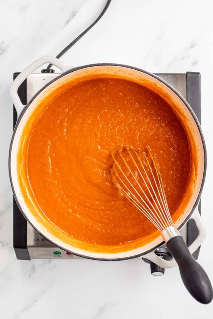 A pot of sauce with a whisk in it.