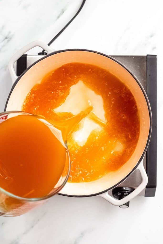 An orange sauce being poured into a pan.
