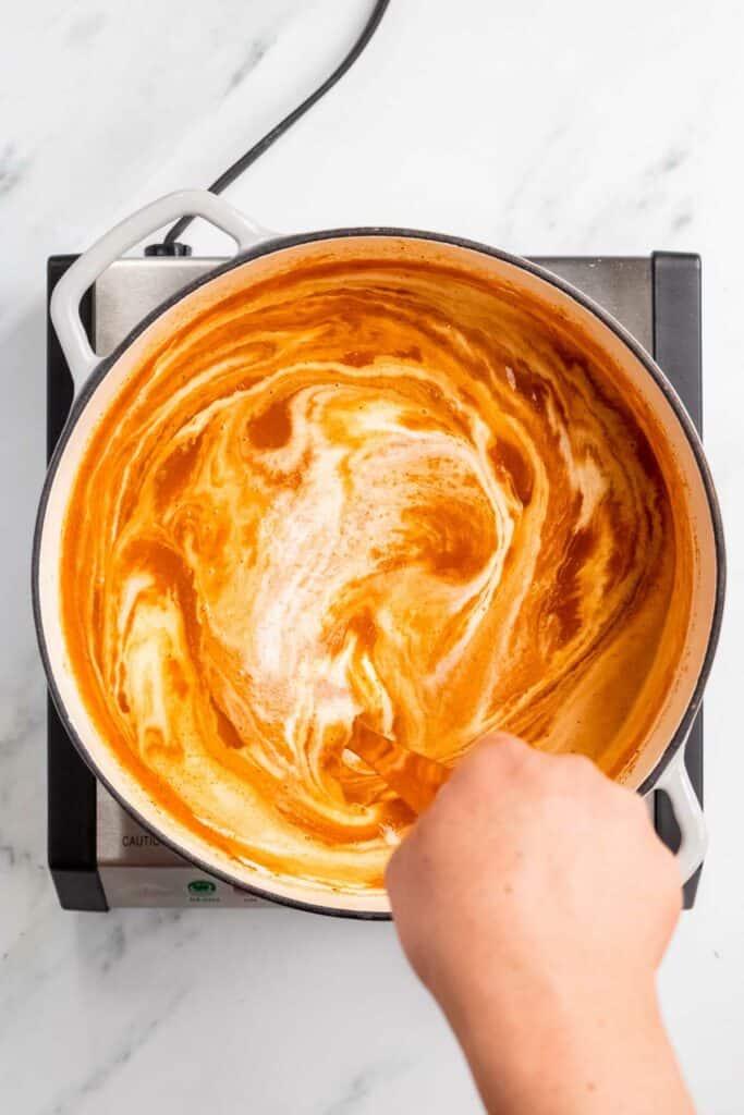 A person stirring a sauce in a pan.