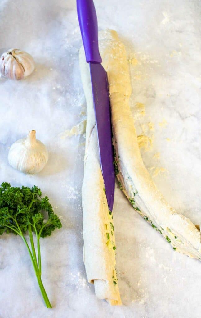 A purple knife is laying on top of a piece of bread with garlic and parsley.