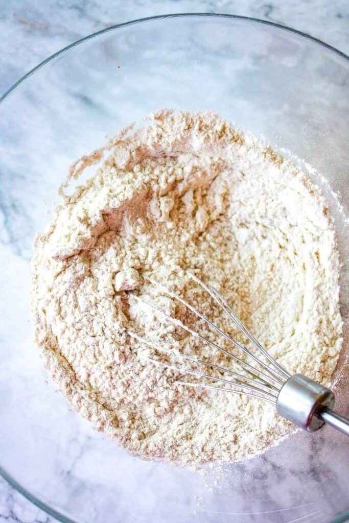 A bowl of flour with a whisk in it.
