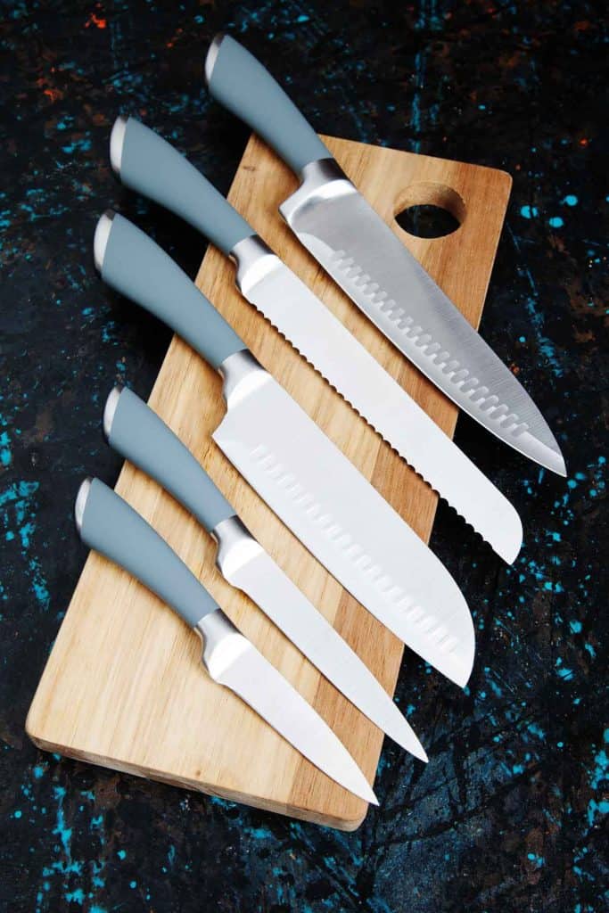 Five knives on a wooden cutting board.