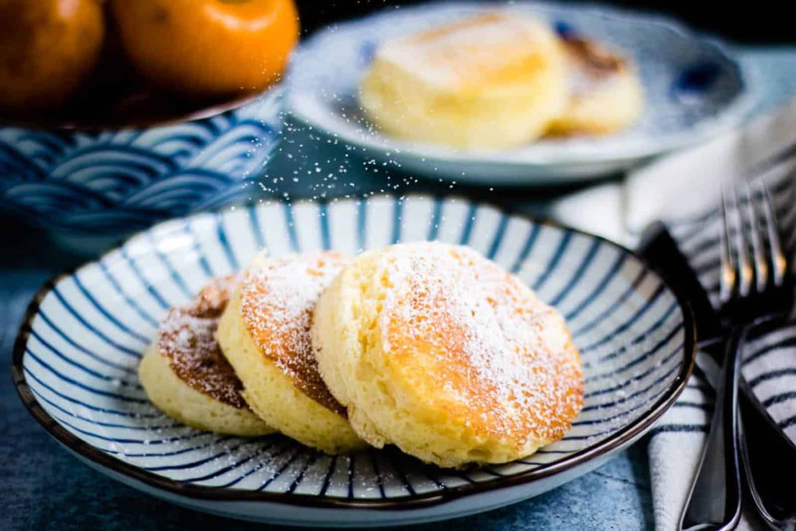 Three souffle pancakes with powdered sugar on a blue and white striped plate.