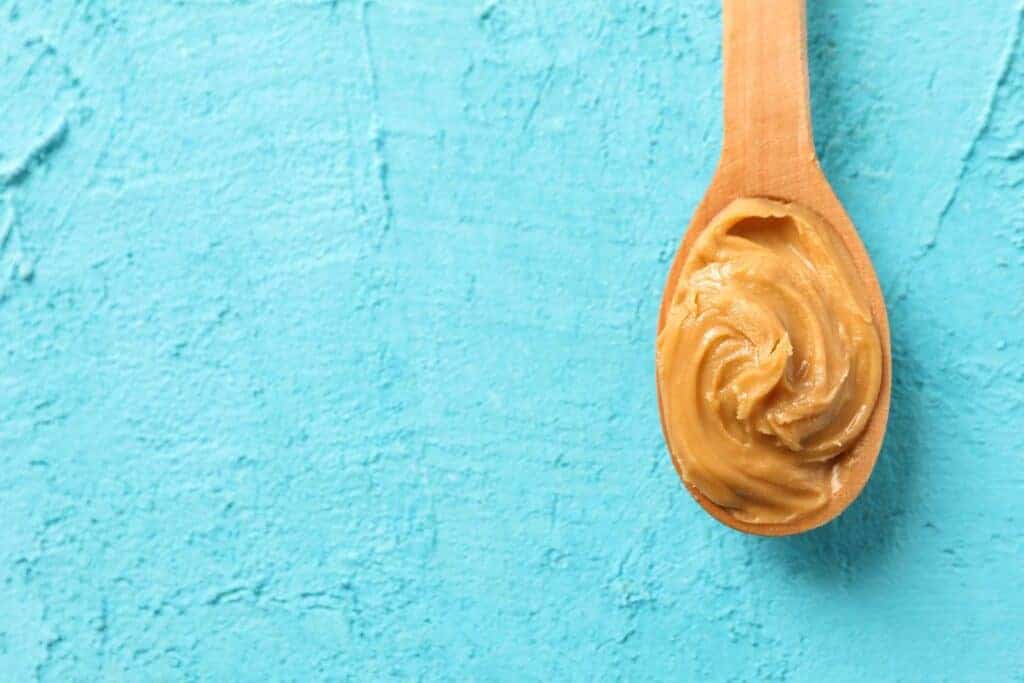 Peanut butter on a wooden spoon on a blue background.