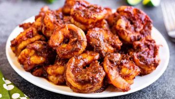 Shrimp in red chile sacue on a plate with limes and forks.