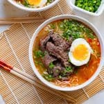A bowl of beef noodle soup with an egg and chopsticks.
