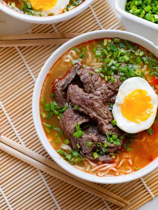 A bowl of beef noodle soup with an egg and chopsticks.