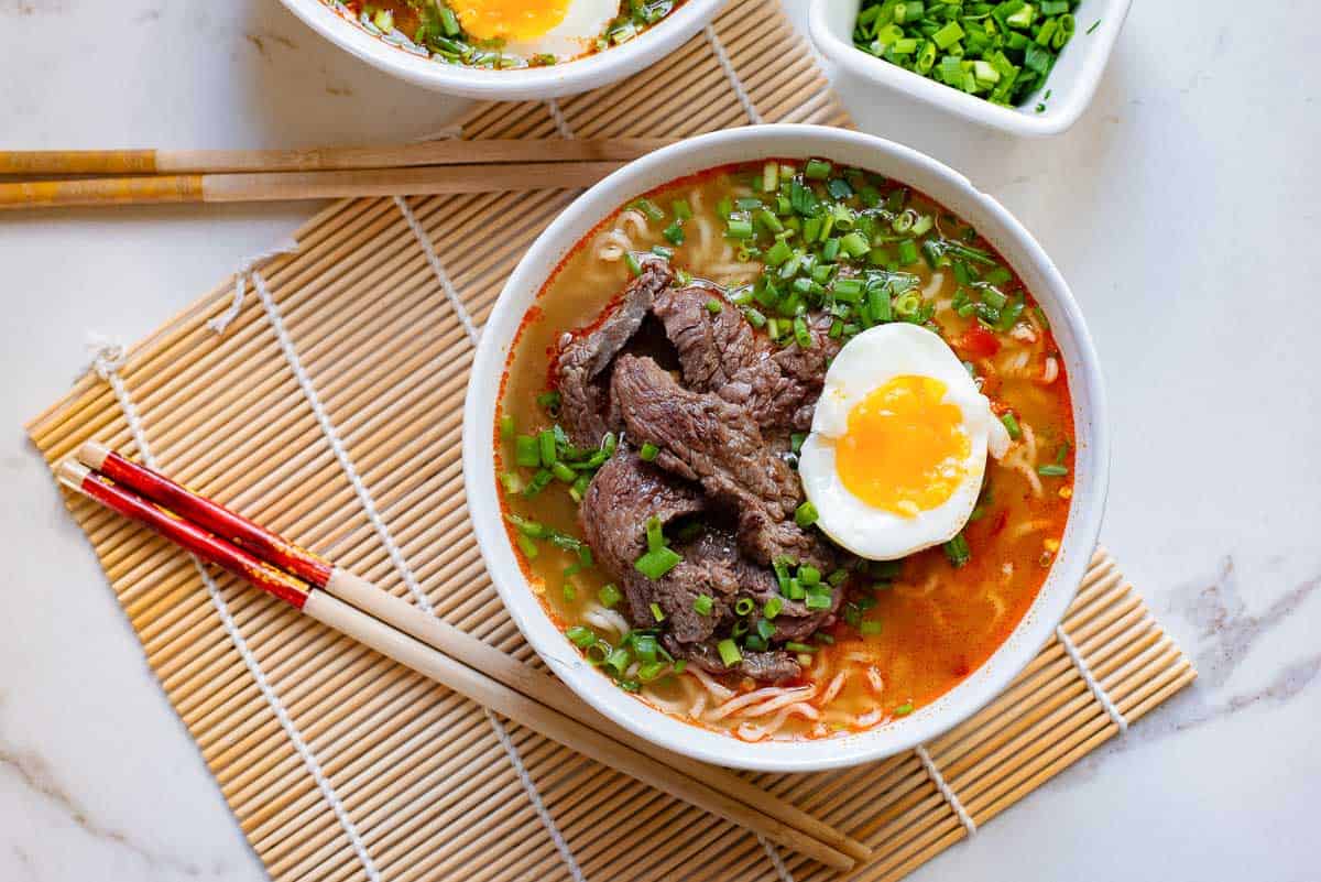 A bowl of beef noodle soup with an egg and chopsticks.