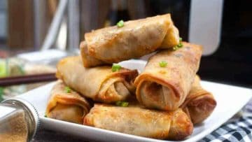 Chinese spring rolls on a plate in front of an Air Fryer for stress-free snacking.