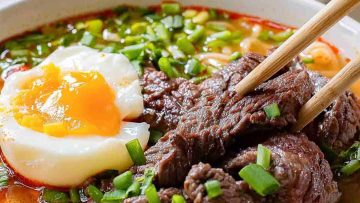 A bowl of beef noodle soup with an egg and chopsticks, perfect for satisfying your craving for Asian noods.