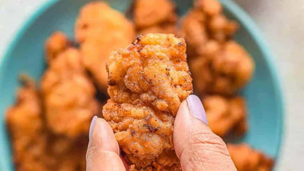 A person holding up a plate of super quick game day snacks, featuring fried chicken nuggets.