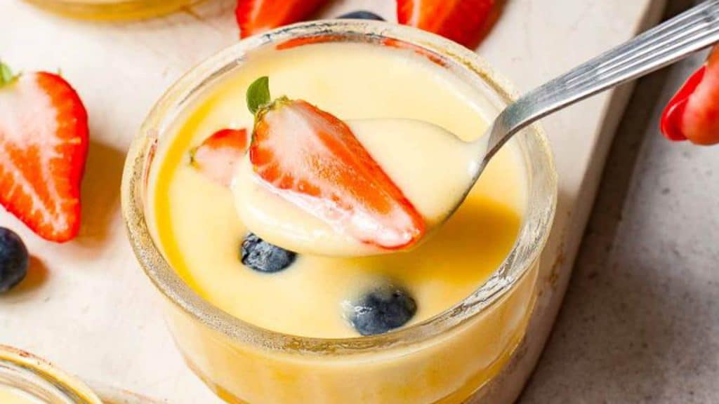 A spoon is being held over a jar of lemon custard with strawberries and blueberries.