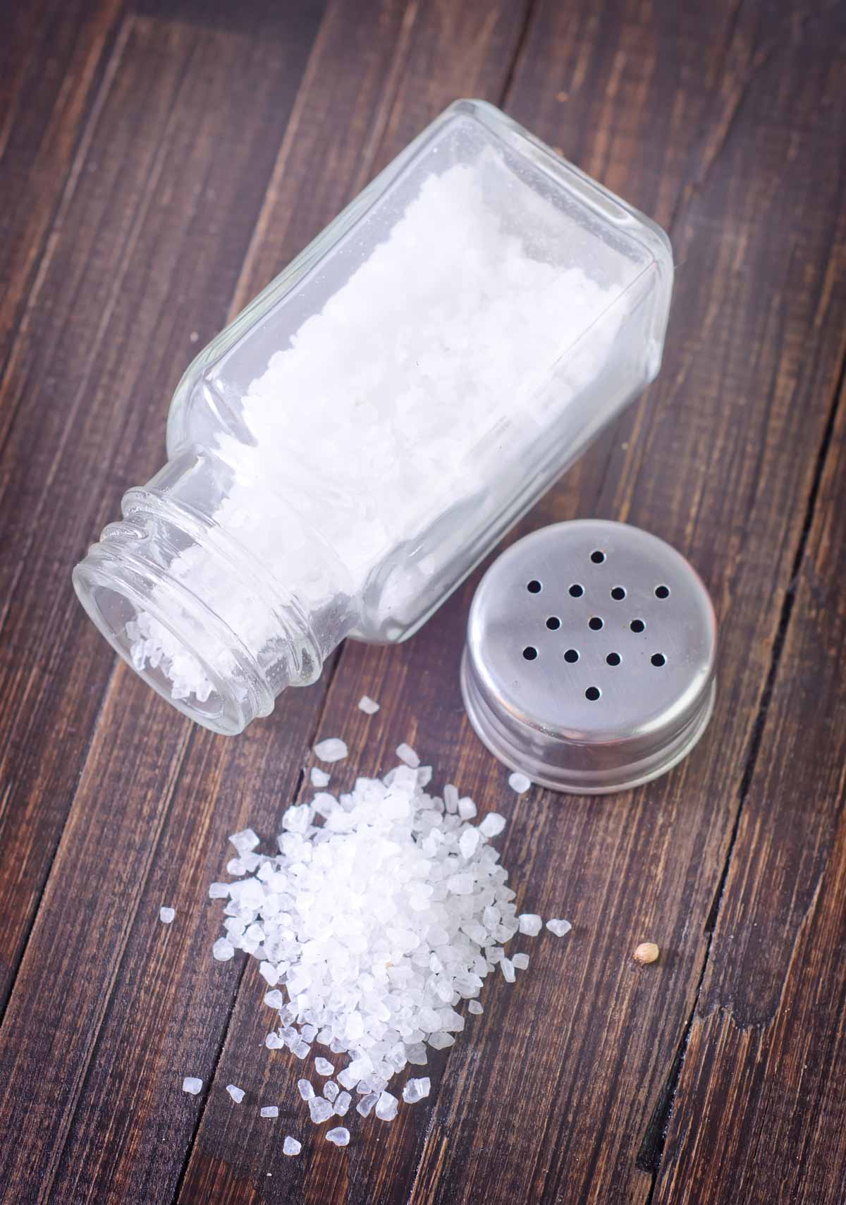 A glass salt shaker and  a salt on a wooden table.