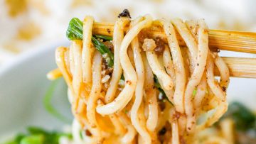 A close-up of twirled spaghetti on a fork, garnished with herbs and bits of meat.