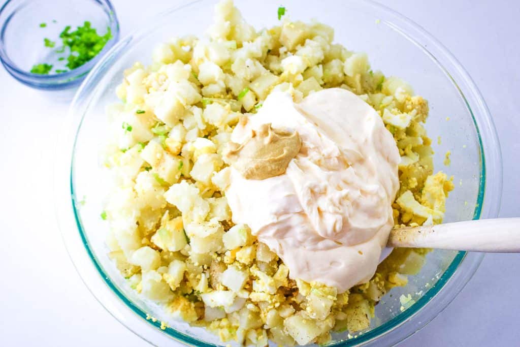 Preparation of potato salad with mayonnaise and mustard being mixed in a glass bowl.