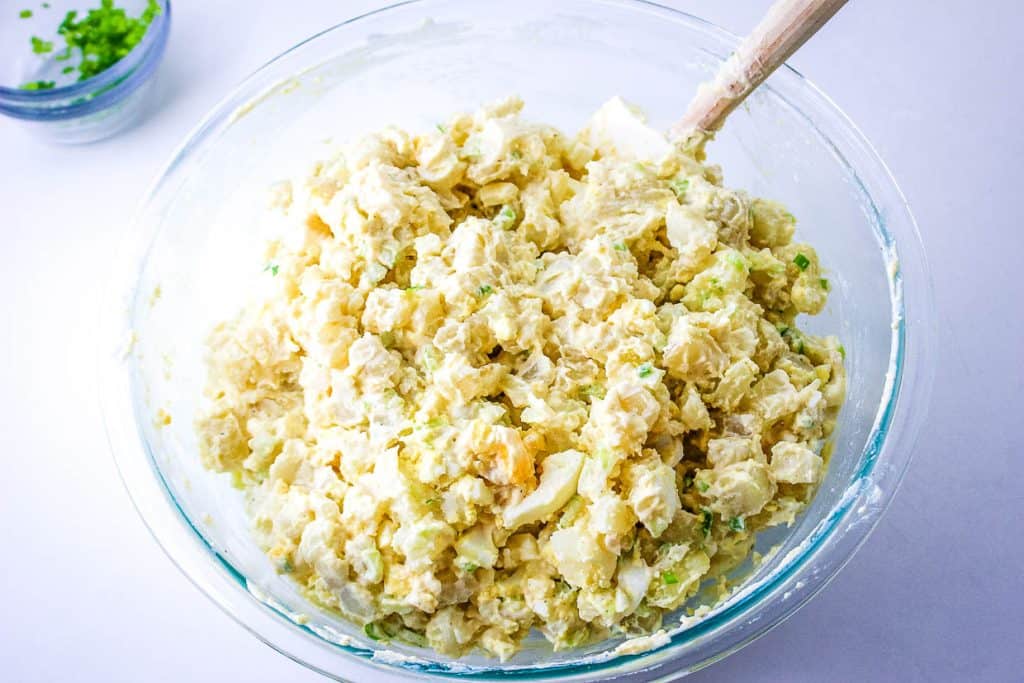 A bowl of potato salad being mixed with a wooden spoon.