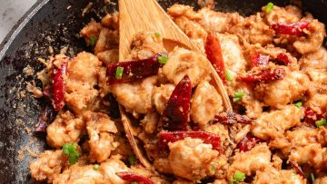 Stir-fried chicken with chili peppers and green onions in a black skillet.