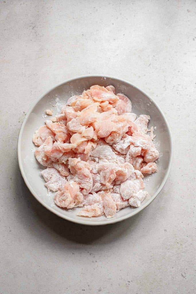Raw chicken pieces dusted with flour on a ceramic plate.