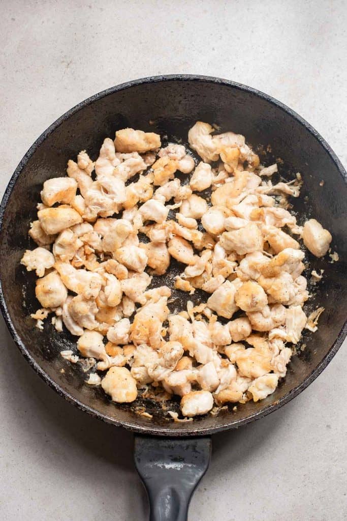 Diced chicken pieces being sautéed in a black cast iron skillet.