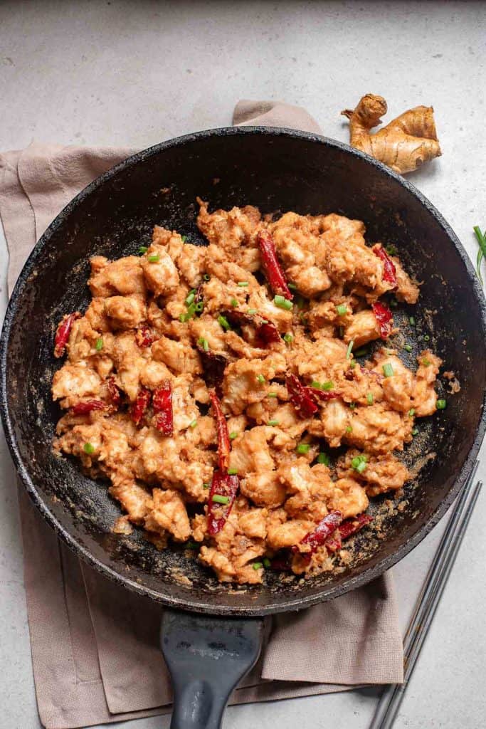 Scrambled eggs with chili peppers and scallions in a black frying pan.