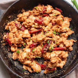 Sautéed spicy chicken dish with spring onions and dried chillies in a black skillet.